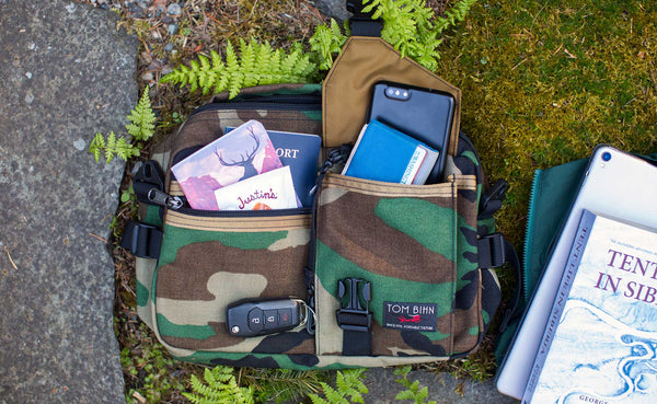 Photo of the LGD in Beaver Camo 1000d. Various items are in it and around it; passport, large phone, wallet, the book "Tent Life in Siberia" and an 11" iPad.